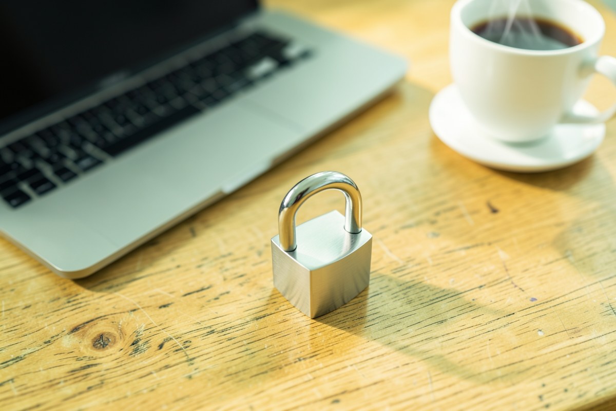 A padlock on a desk with a laptop in the background, representing privacy and security.